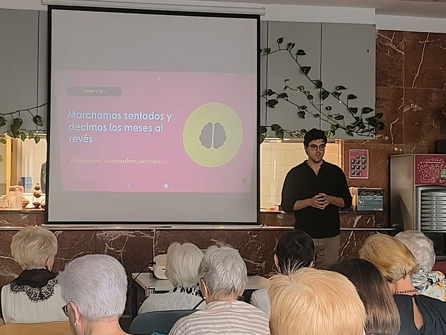 Charla de Altea en un centro de mayores de Pamplona: el ponente explica una prueba de equilibrio y memoria ante el público